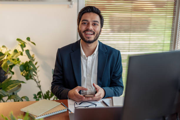 istock Smiling indian businessman in suit use phone while working from home office and looking at camera 1448864987