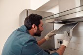 Handyman in uniform repairing kitchen extractor, replacing filter in cooker hood.Maintenance concept