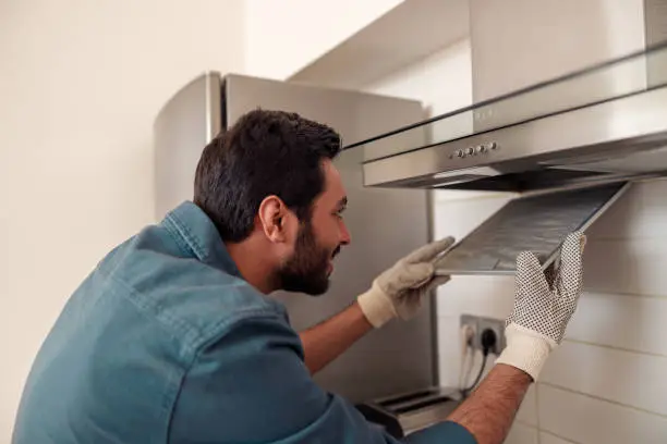 Photo of Handyman in uniform repairing kitchen extractor, replacing filter in cooker hood.Maintenance concept