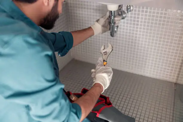 Handyman is repairing faucet of a sink at bathroom. Maintenance and household assistance concept