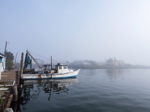 Tapia de Casariego harbor in thick fog, touristic location. Rows of moored fishing boats defocused, stone dock, lighthouse .