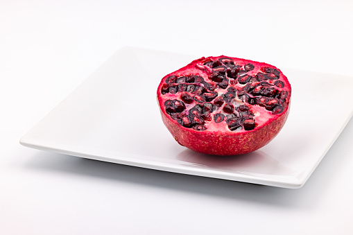 Studio shot of half a pomegranate striking red exposed on a white plate cut out on a white background