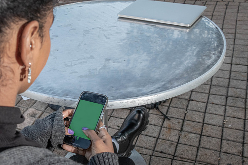 An African American woman uses her smartphone that displays a green screen.  Copy space above and to the right.