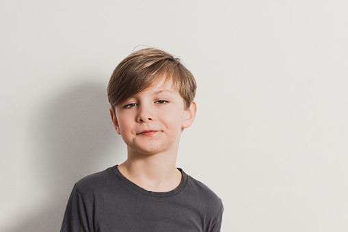 a portrait of cute boy pulling faces, snooty look, dark grey shirt, white wall. Copy space