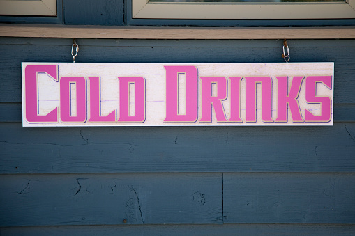 Wooden retail sign at the beach, selling cold drinks.