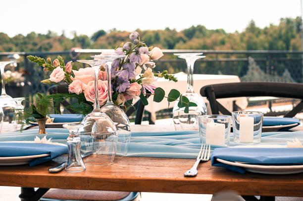 Romantic wedding or another catered event table setting, flowers, white plates, candles, blue napkins, outdoors