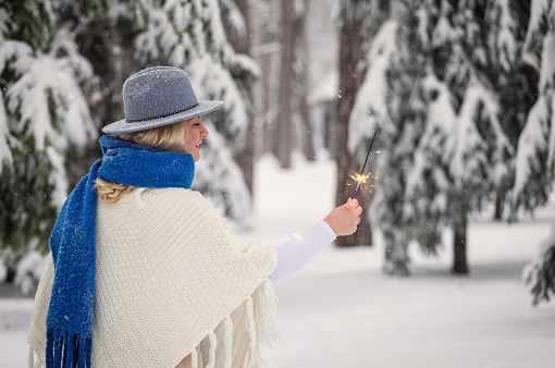 Smiling woman holding sparklers and enjoying on a snowy mountain during Christmas holidays