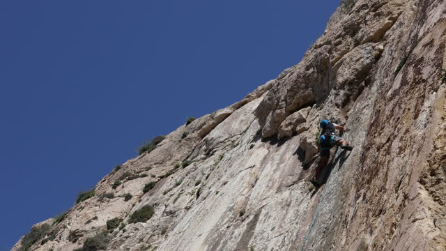 A man leading an active lifestyle climbs a rock, using a climbing rope