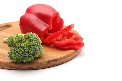 Vegetable concept. Sliced pepper and broccoli on cutting board. White background. Copy space. No people.