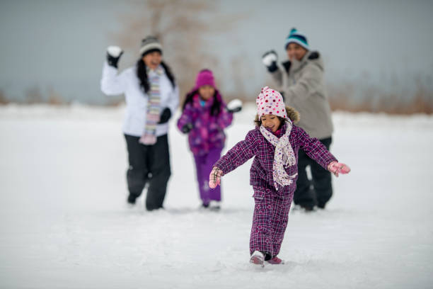 Caucasian girl aged 8-10 years in a pink wollen hat and winter coat snowshoes on a frozen river unaware that her male cousin has fallen behind her in the snow while snowshoeing through the snowy woods in winter, Minnesota, USA
