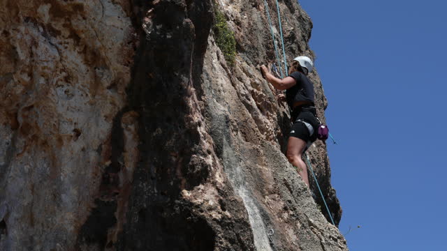 The woman moves forward climbing the steep cliffs of the mountain