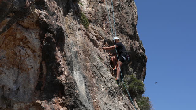 A strong female climber climbs to the top of the mountain using a climbing rope