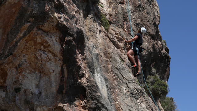 A woman with a protective helmet bravely climbs to the top of the mountain
