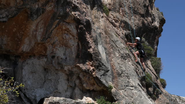 An athletic woman with full climbing equipment climbs a steep cliff