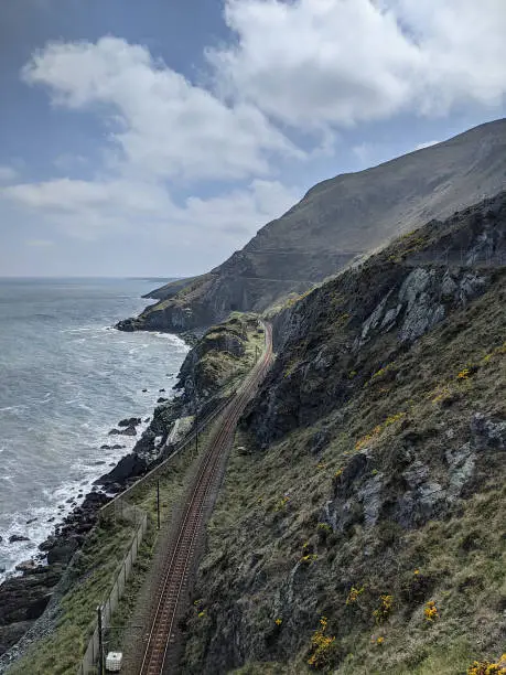 A shot of a railroad. On its left the wide ocean where the waves hit the rocks. On its right the mountains and the cliffs. The train goes its way through an untouched faboulous nature.