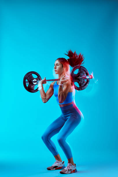 Scatto in studio di una bodybuilder donna che solleva bilanciere. Cattura del movimento a lunga esposizione. - foto stock