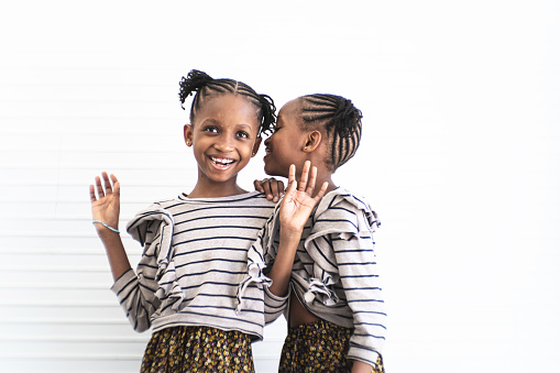 Twin girls whispering into her sister's ears