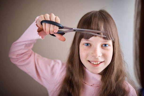 a little girl with freckles and blue eyes with scissors cuts her hair. stock photo
