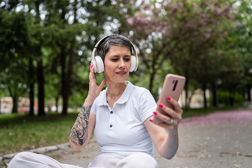 one woman mature caucasian senior female sit outdoor with headphones for guided meditation prepare to meditate front view real people self-care manifestation practice mental emotional balance concept