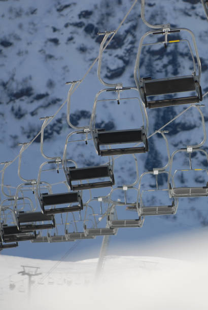 Empty chair lift on a sunny day with snowcovered pine trees and mountainrange in the background in the skiresort St. Anton, Austria.