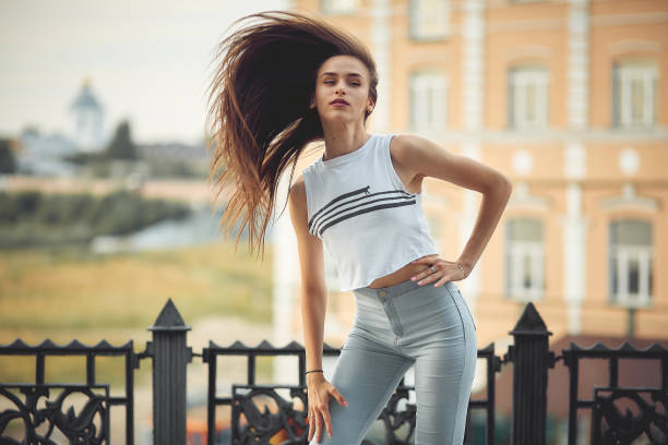 portrait of a girl in jeans and a t-shirt on the background of the building in the evening on a summer day. street dancing in the city stock photo