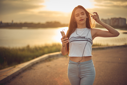 Young beautiful caucasian girl listening to music with smartphone walking in the city with headphones smiling - relax, youth, emancipation concept.