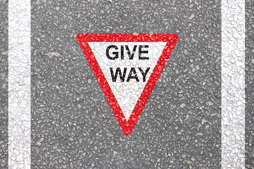 Give Way road Sign for traffic movement control red reverse triangle with written give way message painted on Highway.