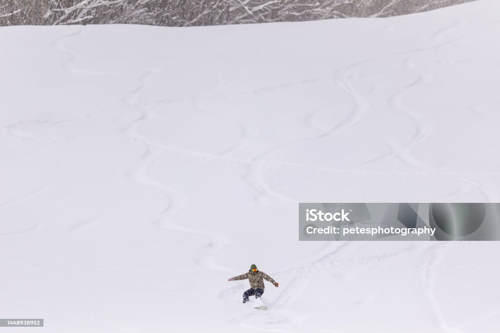 Snowy hill background with snowboarder riding down A view from far of a snowy hill with a man riding down in powder snow - Japan. Iwate Prefecture Stock Photo