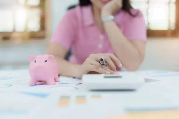 Photo of investment plan, young asian woman keep coin money in jar and using calculator to calculate savings