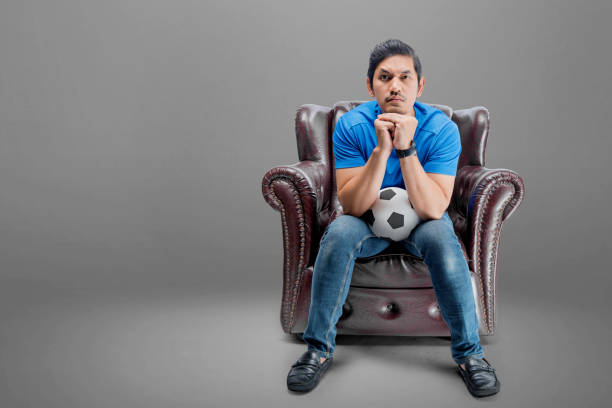 istock Asian man with the ball sitting on the couch with a serious expression 1448944102