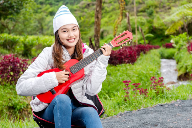 Asian woman playing guitar enjoying camp activity in nature