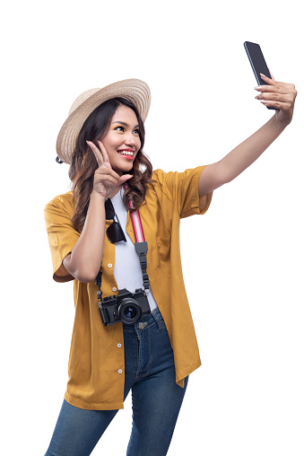 Asian woman with a hat and camera taking a selfie with a mobile phone isolated over white background