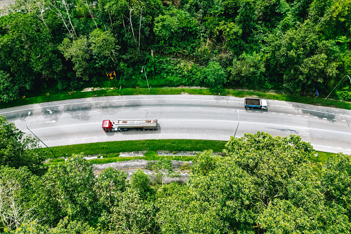 from drone point of view, truck passing by a curve road with forest at both side