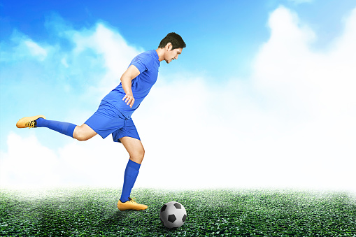 Asian football player man in a blue jersey kicking the ball on the football field