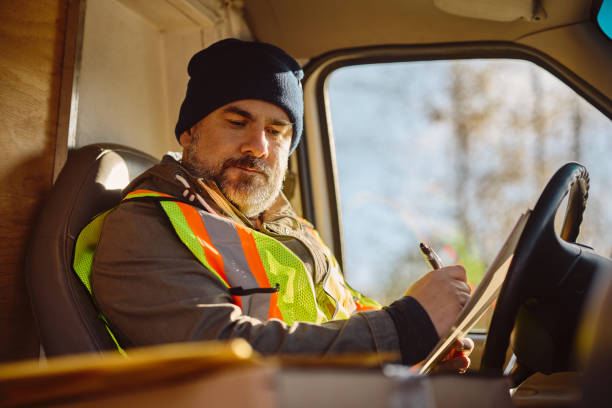 istock Delivery man writing on clipboard while checking packages in truck cabin. 1448958335