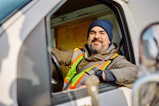 Portrait of happy professional truck driver looking at camera through side window.