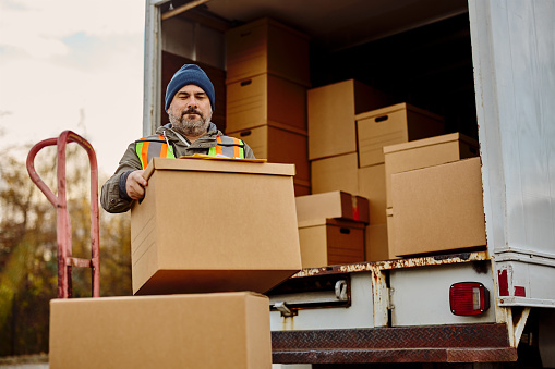 Mid adult courier loading delivery boxes for shipment into a truck.