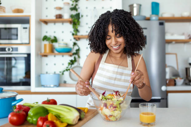 sain. bonne vie. des aliments biologiques. légumes. fermez le portrait de la belle jeune femme heureuse mignonne tandis qu’elle essaye la salade vegan savoureuse dans la cuisine à la maison. - nutriment photos et images de collection