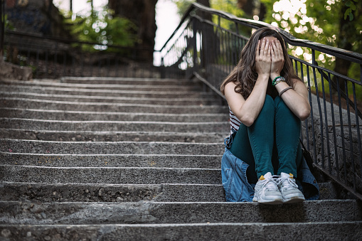 Depressed young woman covering her eyes while sitting on stairs