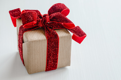 Gift box wrapped in brown paper and red velvet ribbon on white table