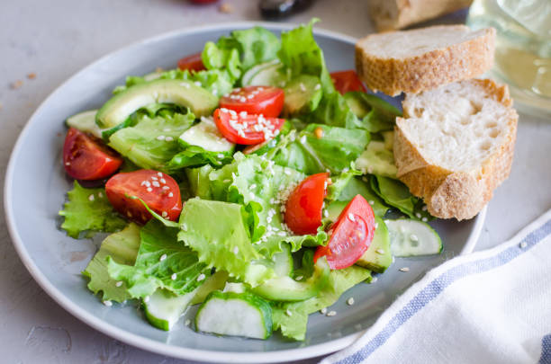 Fresh green organic salad with raw ingredients close up. Tasty salad with lettuce, cherry tomatoes, cucumbers, greens and onions on grey plate for lunch, top view. Healthy eating, dieting concept