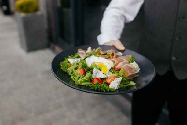 istock Delicious salad - jamon, cheese, egg and fresh vegetables on a gray background. Man holding a plate of salad. Salad in a restaurant. Healthy food. Copy space. 1448992155