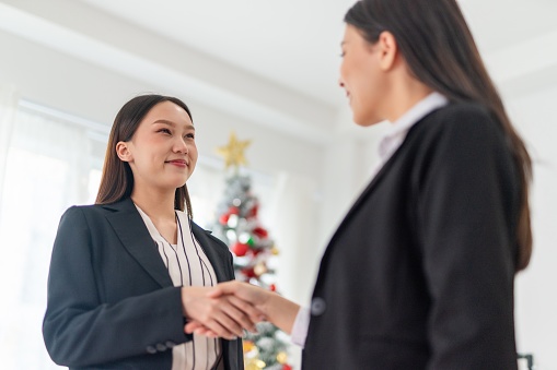 Feminism power. Two young smart beautiful asian lady businesswomen smiling and have a hand shake to commemorate a deal successful in front of a nicely decorated Christmas tree in a meeting room