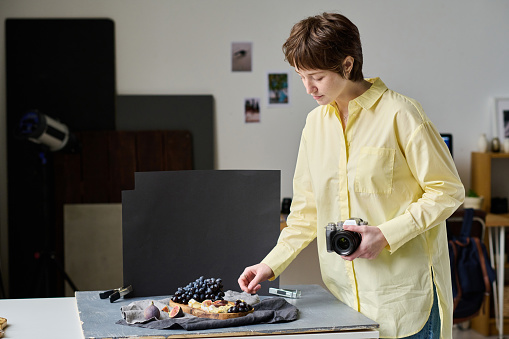 Young photographer decorating dish with fruits for professional shooting on camera in studio