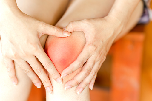 A woman brings her hand to her knee because of pain. Health care concept.