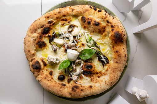 Neapolitan pizza with anchovies and mozzarella on the marble table with leaves and statues