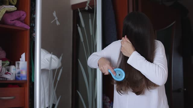 The woman brushes her hair in front of a mirror.