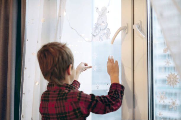 istock Little cute caucasian boy decorating window with christmas stickers. 1448999873