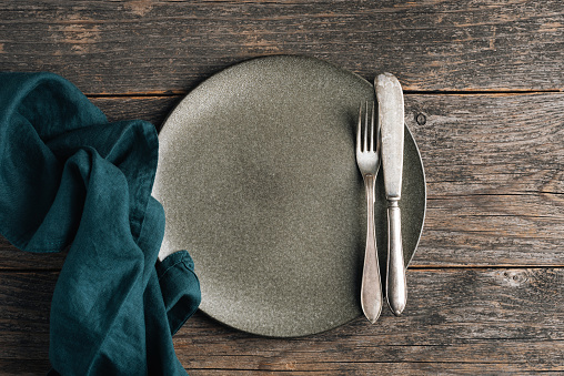 Vintage silverware and empty green plate on a wooden table background. Dining table setting. Top view