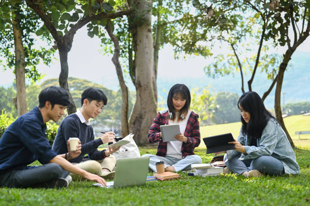 istock Young Asian college students working on group project and communicating while sitting on on campus lawn on beautiful day. 1449007866